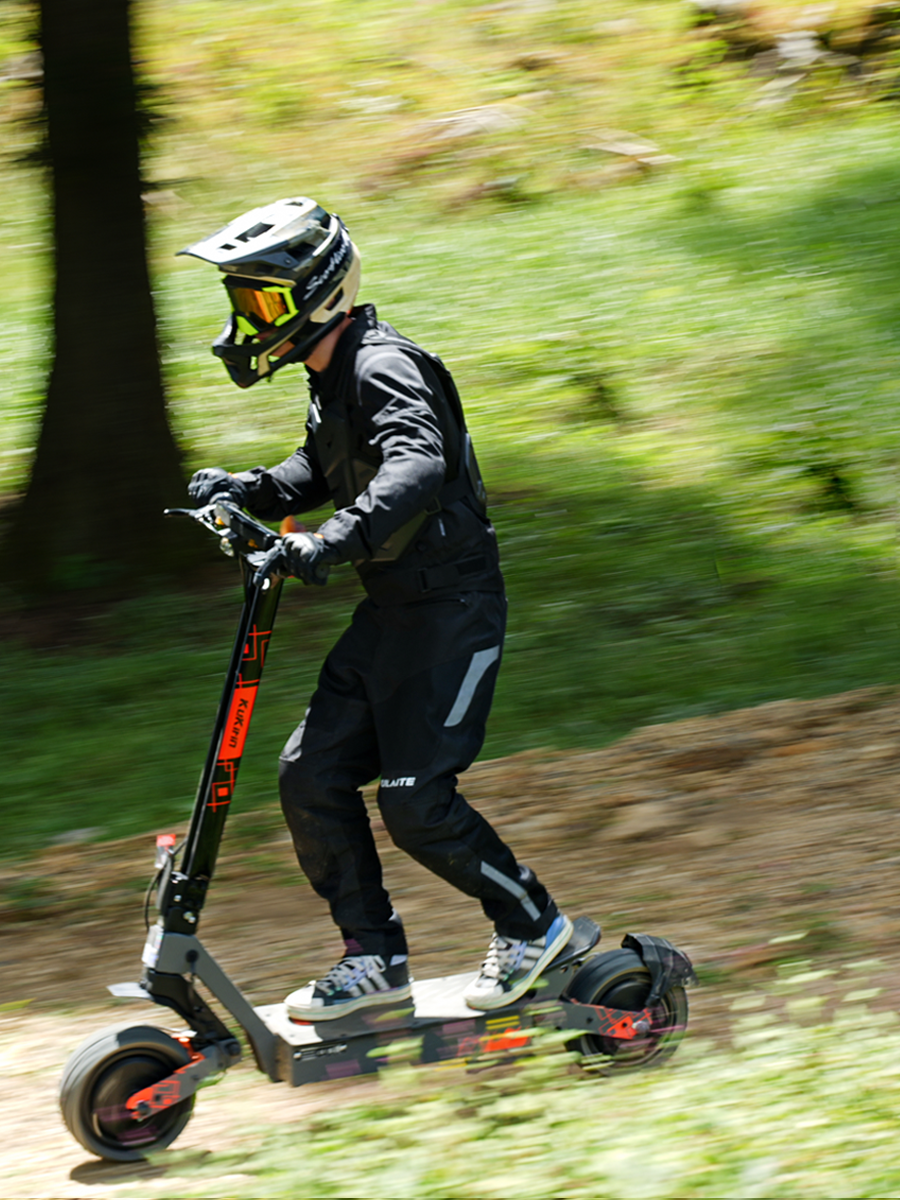 Rider wearing protective gear riding the KuKirin G4 Ultra all-terrain electric scooter on a forest trail